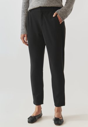 Black tapered pants made of soft fabric, featuring side pockets, a front button closure, and a smooth texture. Worn with black flats.