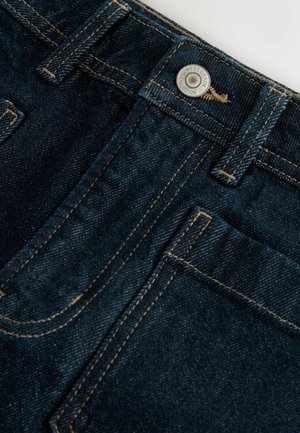 Mörkblå denimjeans med gyllene sömmar, med en framficka, knäppning och en etikett på midjebandet. Strukturerad tyg.