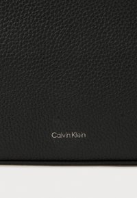 Černá peněženka z texturované kůže s jemným stříbrným logem Calvin Klein. Povrch vykazuje zrnitý vzor pro zvýšení detailu.