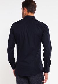 Camisa de manga larga navy con cuello clásico, textura suave, puños con botones y un corte entallado, costuras visibles y detalles en la parte trasera.