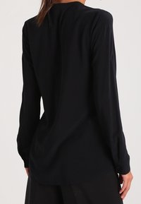 Haut noir à manches longues avec une texture lisse et une coupe décontractée. Présente de légères fronces aux épaules et un ourlet incurvé.