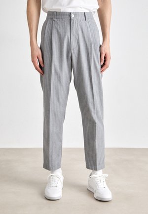 Gray striped trousers with a pleated front, button closure, and tapered legs, paired with white sneakers, shown on a neutral background.