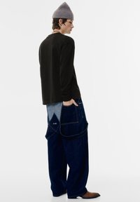 Zwart T-shirt met lange mouwen, losvallende blauwe spijkerbroek-met-lapjes met lichter denimaccent, grote zakken en een gestructureerde grijze beanie.
