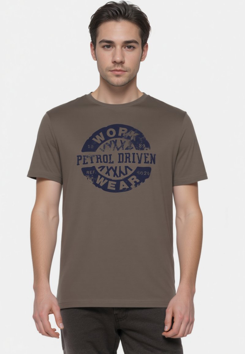 Brun bomulds T-shirt med et cirkulært navy grafisk design med teksten "WORK" og "PETROL DRIVEN." Rund hals og korte ærmer, glat tekstur.