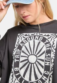 Schwarz langärmliges Shirt mit einem großen weißen Sonnengrafik und stilisiertem Text. Der Stoff wirkt weich mit einer lockeren Passform und rundem Ausschnitt.