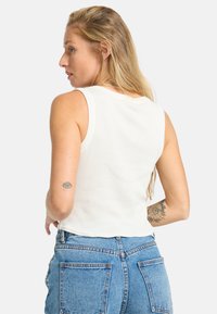 Hvid ribbet tanktop med en tætsiddende design, der har brede skulderstropper og en cropped længde, parret med højtaljede blå denimjeans.