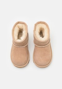 Botas de tobillo de gamuza marrón con un suave revestimiento de piel de fur, punta redonda y detalle trenzado en la parte superior. Suela de goma plana para mayor tracción.