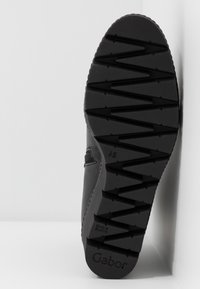 Semelle de chaussure noire avec des crampons en zigzag profonds et le nom de la marque "Gabor" visible près du talon.