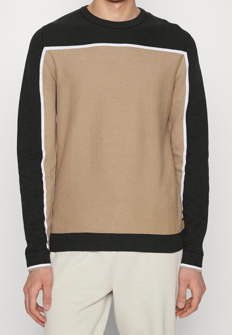 Maglione lavorato a maglia con un design a blocchi di colore, corpo beige, maniche nere e dettagli bianchi lungo le cuciture. Collo rotondo, tessuto testurizzato.