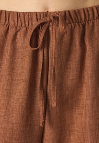 Shorts en lin marron avec une taille élastique, cordon de serrage réglable et une finition texturée. Présente un design simple et décontracté.