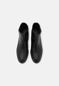 Musta nahkasaappaat nilkkapituisena, joissa on tyylikäs muotoilu, pyöreä kärki ja joustavat sivupaneelit. Liukas pinta ja tasapohja. Ei näkyvää varustusta.