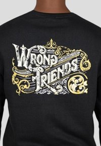 Svart sweatshirt med utsmyckad vit och guld text som säger "WRONG FRIENDS," med invecklade detaljer och mönster genom hela.
