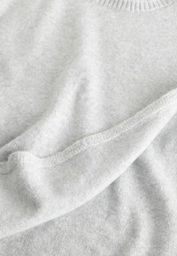 Tissu tricoté gris clair doux avec col côtelé visible et détail de bord plié, mettant en valeur la texture et les coutures.