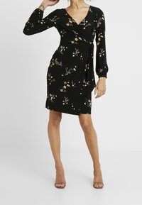 Svart omslagsklänning med V-ringning, långärmad, blommönster i gult och vitt, sidoknytning och knäskuret.