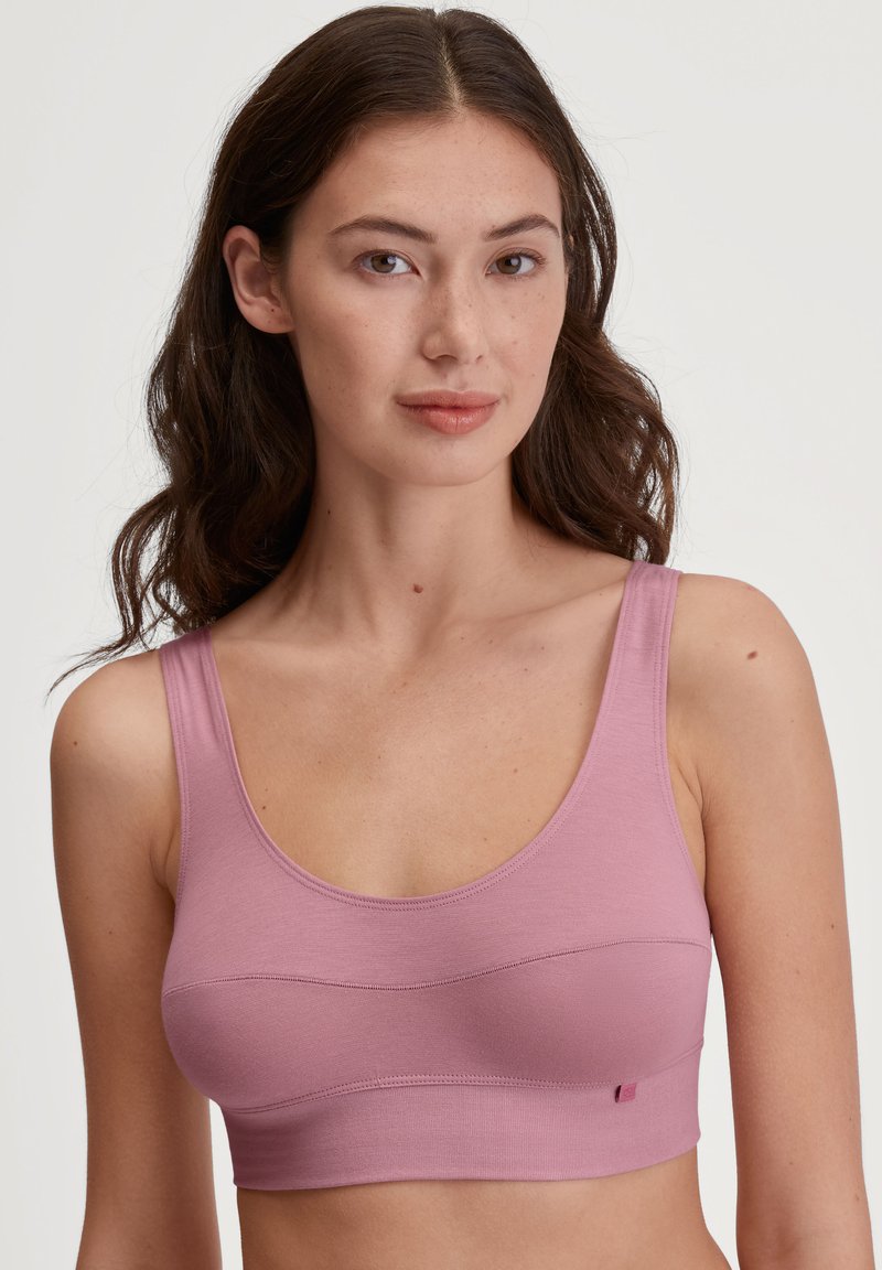 Helles rosa Sport-BH mit breiten Trägern, Rundhalsausschnitt und enganliegendem Design. Verfügt über genähte Akzente auf der Vorderseite und eine glatte Textur.