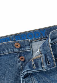 Denim jeans with a light blue wash, featuring copper-toned hardware, blue logo on the waistband, and contrasting stitching details.