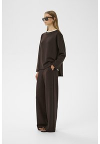 Top marrón de manga larga con cuello blanco, combinado con pantalones marrones sueltos. El conjunto tiene un ajuste relajado y está hecho de una tela suave y texturada.