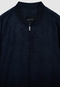 Marineblaue Bomberjacke mit glatter, wildlederartiger Textur. Verfügt über einen gerippten Kragen, einen Frontreißverschluss und Seitentaschen. Markenetikett innen sichtbar.