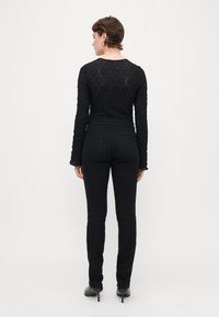 Melnas mežģīņu krekls ar garām piedurknēm, kas izceļ teksturētu rakstu, apvienots ar augsto jostasvietu melnām džinsām. Abi apģērbi ir pieguļoši un eleganti.