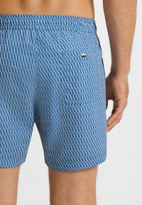 Blå mönstrade badshorts med vågdesign, resår i midjan och en bakficka med en liten märkt etikett.