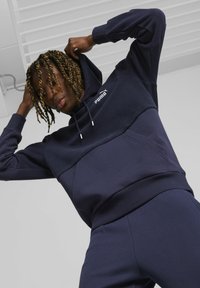 Sudadera con capucha de color azul marino hecha de tela suave, con un bolsillo tipo canguro, capucha y el logo blanco de Puma en el pecho; diseño texturizado con panel contrastante.