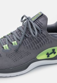 Šedá sportovní bota s texturovaným svrškem, kontrastními zelenými akcenty, kulatými šněrovadly a bílou podešví se skvrnitým vzorem.