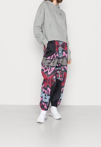 Sudadera gris corta con un logo, combinada con pantalones de chándal de colores y estampados que presentan gráficos en rosa, negro y azul. Zapatillas deportivas blancas.