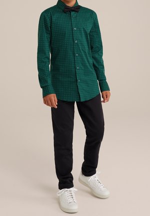 Zelená košile na knoflíky s malými bílými puntíky, dlouhými rukávy a černým motýlkem. Kombinováno s černými kalhotami a bílými teniskami.