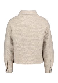 Veste beige raccourcie en tissu texturé avec un subtil motif en chevrons, dotée d'un col et de poignets à boutons.