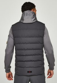 Grijze gewatteerde vest met capuchon, voorzien van horizontale stikpatronen. Het heeft een gladde textuur en logo-accenten op de rug en zoom.