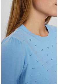 Gaiši zila adīta džemperis ar apaļu izgriezumu un smalku mazu caurumu rakstu visā audumā. Mīksta tekstūra, ribinātas piedurknes.