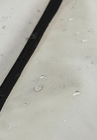 Des gouttes d'eau perlant sur un tissu imperméable gris clair avec une couture noire verticale, mettant en évidence la capacité de répulsion de l'eau et la texture du tissu.
