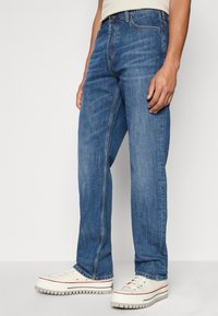 Blue denim straight-leg jeans with a medium wash, featuring a classic five-pocket design. Paired with white sneakers with rubber soles.