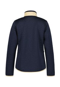 Marinblå quiltad jacka med geometrisk textur, med en kontrasterande beige krage och kant. Långa ärmar och en rundad nederkant fulländar designen.