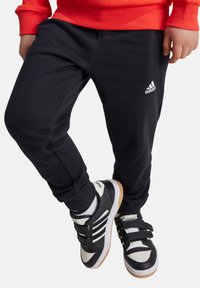 Pantalones de baloncesto negros en una tela suave con un diseño ajustado, que cuentan con un logotipo de Adidas bordado en blanco en el muslo.