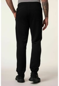 Czarne dresy wykonane z miękkiego materiału charakteryzują się zwężającym się krojem, elastycznym paskiem w talii oraz tylną kieszenią. Noszone z czarnymi butami sportowymi.