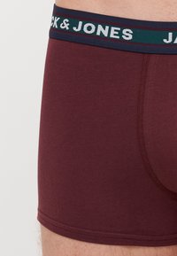 Bordeauxfarbene Boxershorts mit einem elastischen marineblauen Bund, versehen mit einem gewebten "JACK & JONES"-Logo und einer glatten Textur.