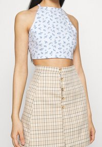 Blomstrande halterneck crop-top i ljusblått med små blå blommor; matchad med en beige och brun rutmönstrad kjol med knapfront och A-linjeform.