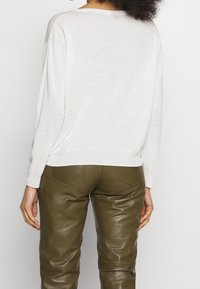 Maglione a maniche lunghe di colore crema realizzato in tessuto leggero, caratterizzato da una vestibilità comoda, abbinato a pantaloni in pelle aderenti di colore verde oliva.