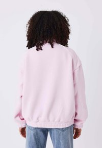Lichtroze oversized sweatshirt met hoge kraag, geribde zoom en manchetten. Zacht materiaal, minimalistisch ontwerp en een nette afwerking.