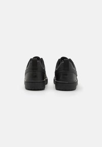 Schwarze Sneaker mit einem glatten synthetischen Obermaterial, gepolstertem Schaftrand und strukturiertem Gummilaufsohle. Sie verfügen über ein schlichtes Design und ein Logodetail an der Ferse.