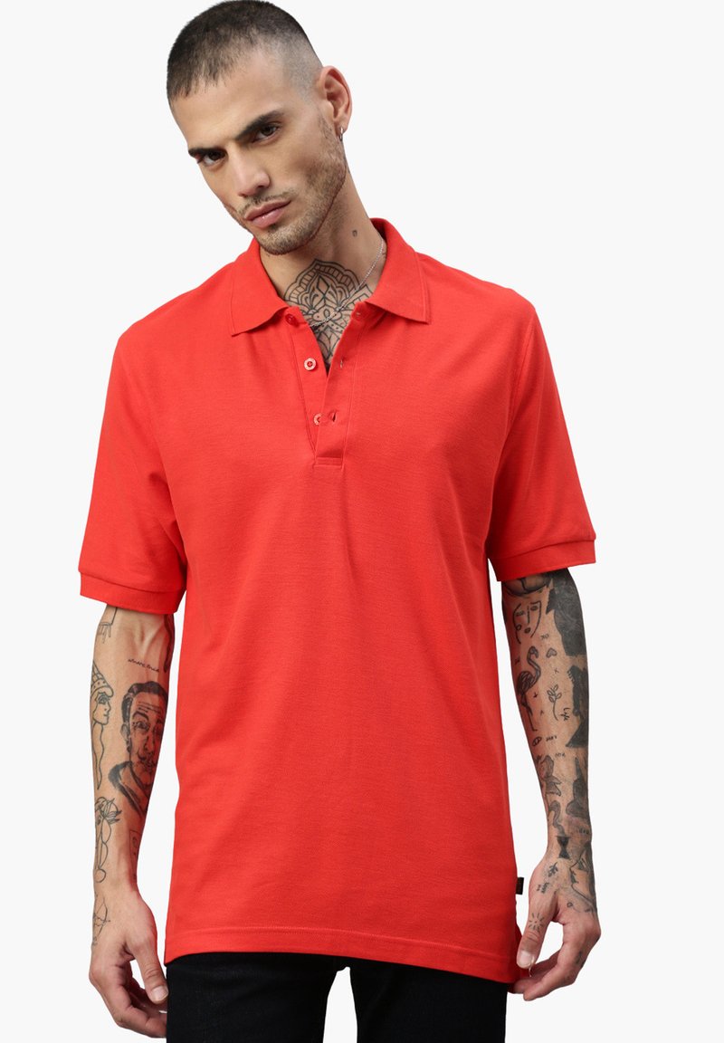 Polo rouge en tissu lisse, dotée d'un col traditionnel, d'une patte de boutonnage à trois boutons et de manches courtes. Design simple sans motifs.