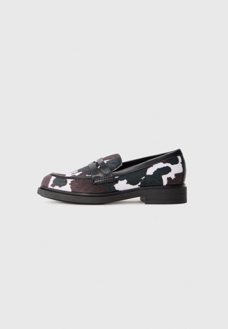Chaussure mocassin avec motif en cuir de vache noir, blanc et brun foncé, bride en cuir noire et talon bas empilé sur fond blanc.