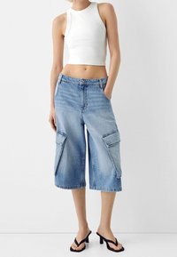 Vaaleansiniset farkku cargo-shortsit, joissa on löysä istuvuus ja polvipituus, sivutaskut ja hillitty kulutus. Yhdistetty valkoiseen lyhytpuraiseen toppiin.