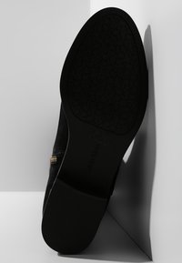 Black suede ankle boot with a patterned rubber sole, gold zipper detail, and smooth texture; curved silhouette enhancing style.