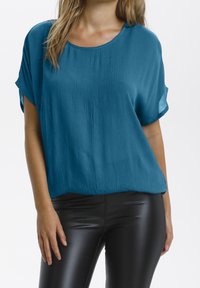 Maglietta corta a maniche con finitura texturizzata in tono teal, dalla vestibilità rilassata e scollo rotondo, abbinata a leggings neri aderenti.