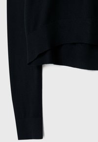 Pull en maille bleu marine foncé avec ourlet et poignets côtelés, montrant un gros plan sur la texture du tissu superposé et le détail de la manche.
