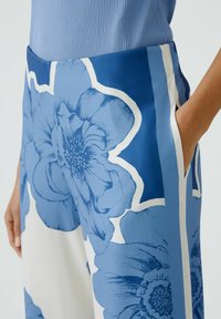 Blaue, floral gemusterte Hosen mit kräftigen weißen Umrandungen und Seitentaschen. Hergestellt aus einem glatten, leichten Stoff.