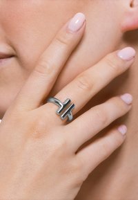 Sølvmetallring med geometrisk design og en delt, rektangulær aksent. Glatt finish, rund ring, båret på en hånd med nøytral neglelakk.