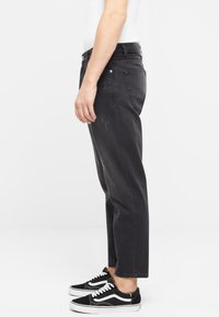 Jeans de mezclilla negros con un corte relajado, que presentan un ligero desgastado, bolsillos laterales y se combinan con zapatillas en blanco y negro.